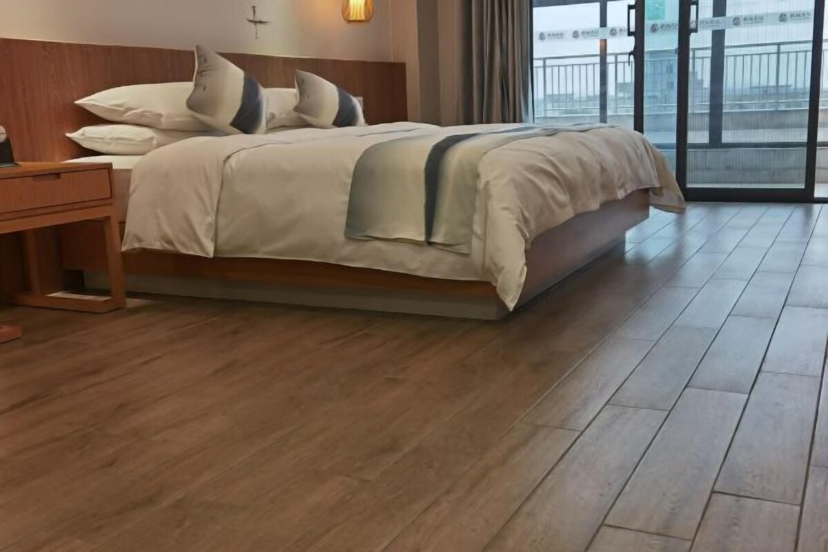 Une chambre d’hôtel avec un lit, un plancher en bois et une vue sur l’extérieur, visible à travers une porte vitrée.