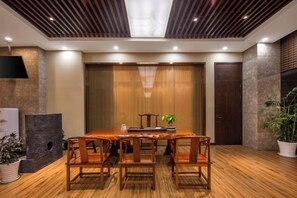 Un salón de conferencias con una mesa y sillas de madera, una planta en maceta y un amplio ventanal al fondo.