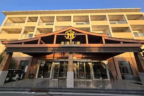 Entrada de un hotel con un logotipo destacado, un área de acceso cubierta y un edificio de varios pisos al fondo.
