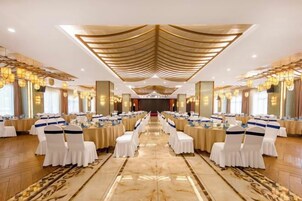 Un salón de banquetes con filas de mesas, sillas y un pasillo central.