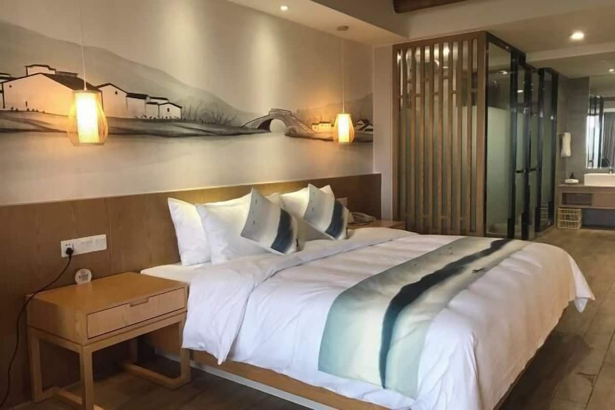 Una habitación de hotel moderna con una cama grande, una mesita de noche, una obra de arte colgada en la pared y un panel de vidrio.