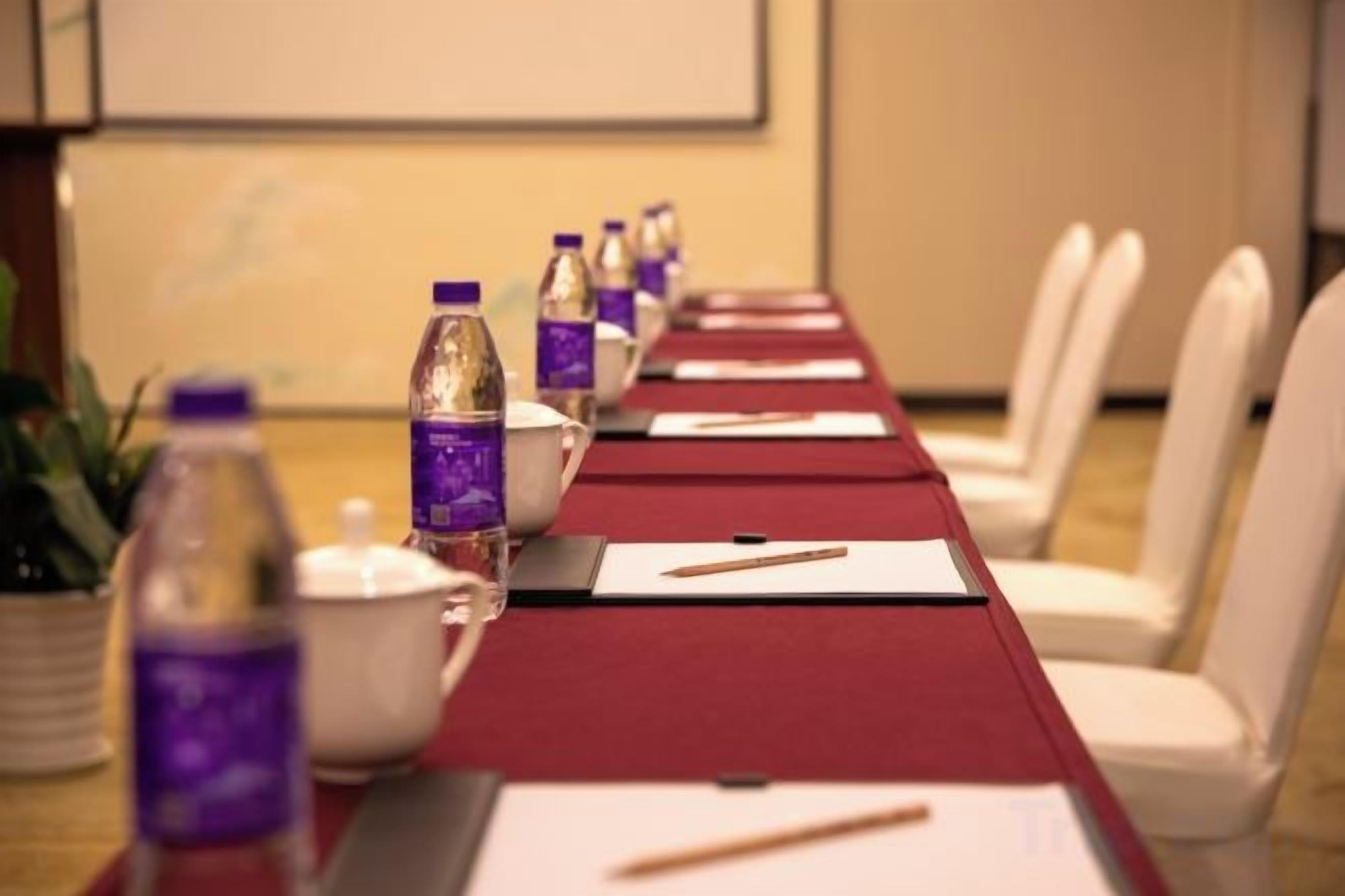 A conference room with a long table, chairs, water bottles, and a projector screen.