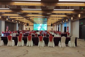 Ein Konferenzraum mit Reihen von Tischen und Stühlen, eine große Leinwand vorne und ein Bühnenbereich.