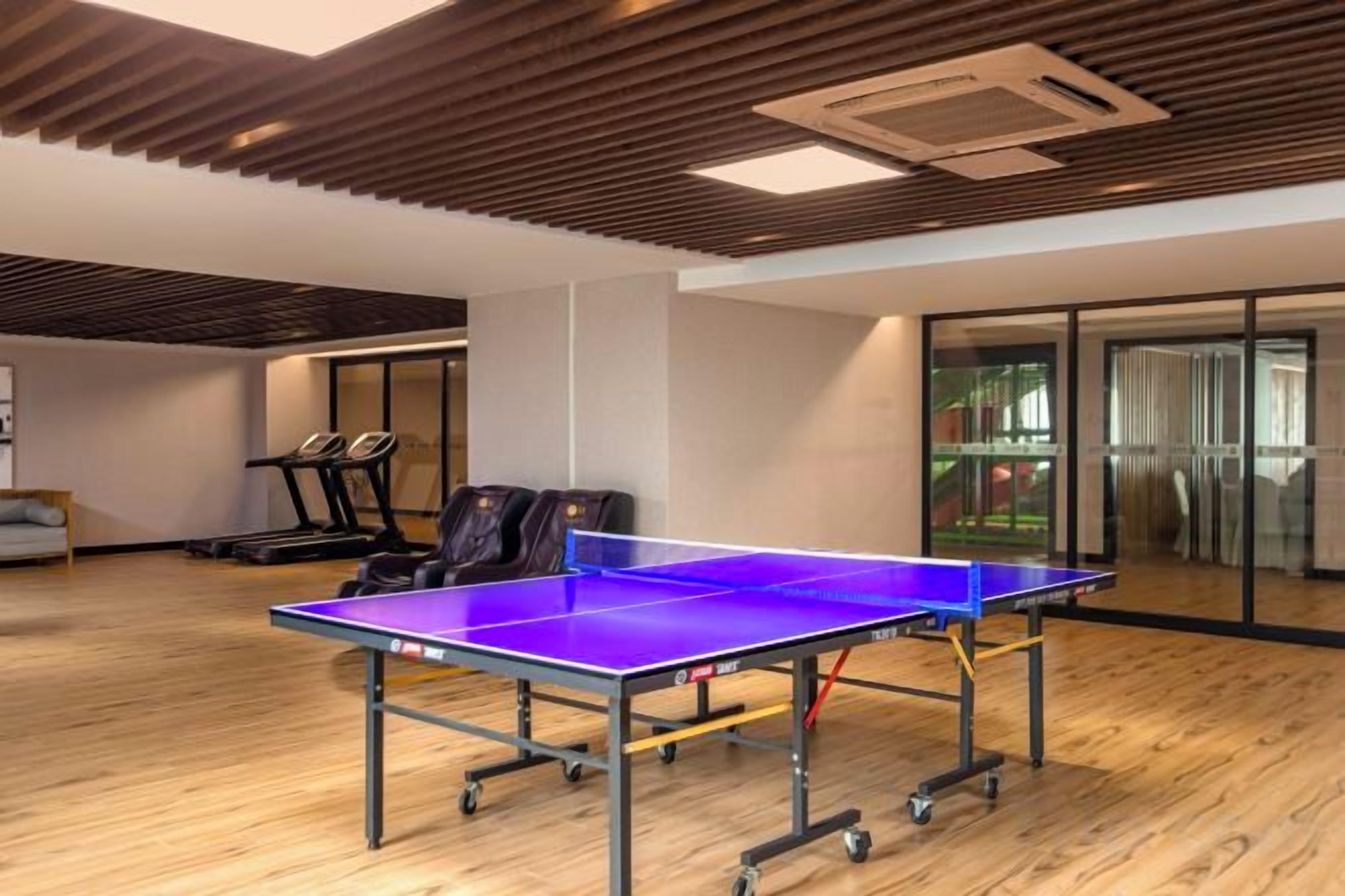A ping pong table in a room with wooden flooring, a treadmill, and a glass wall.