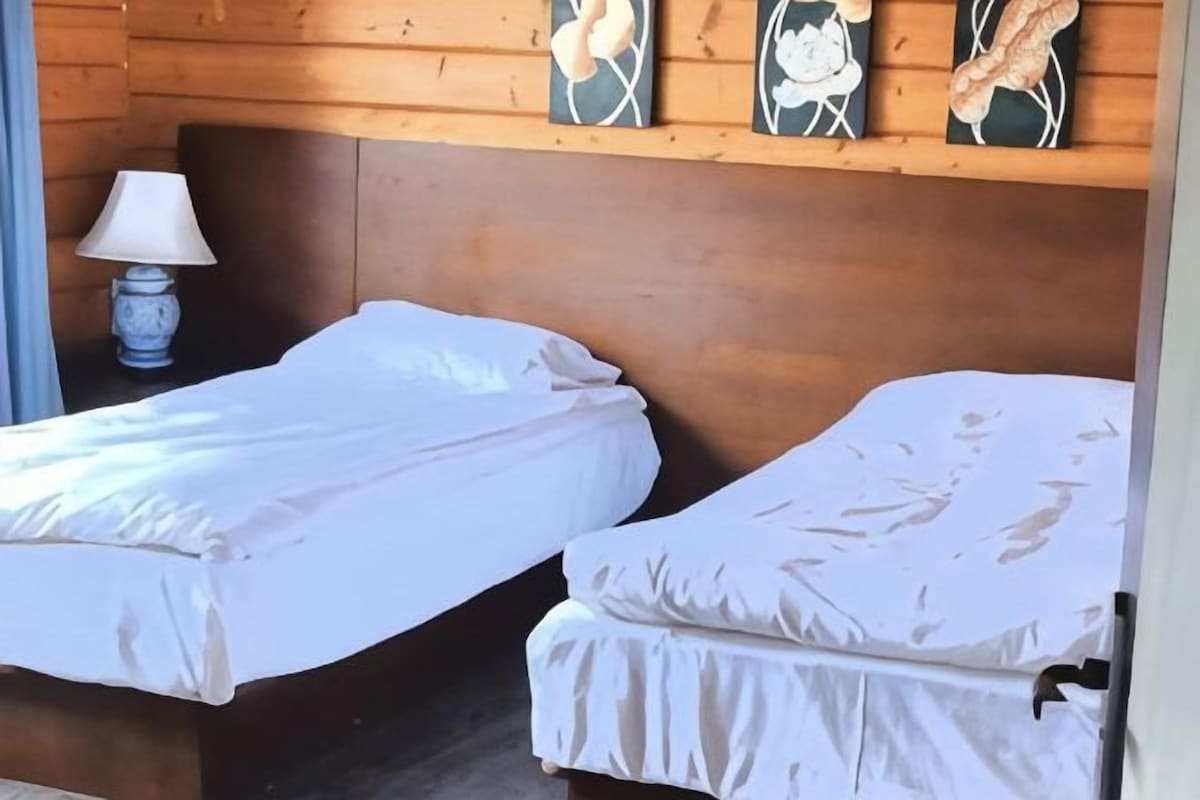 A room with two single beds, a wooden headboard, and a lamp on a nightstand.