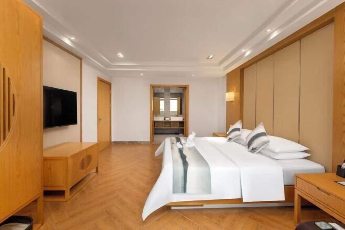 Una habitación de hotel moderna con una cama grande, muebles de madera, un televisor de pantalla plana y vistas al pasillo.