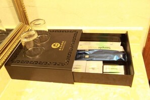 A hotel room with a large mirror, a black box with a logo, and a drawer with various items including a blue package and some papers.