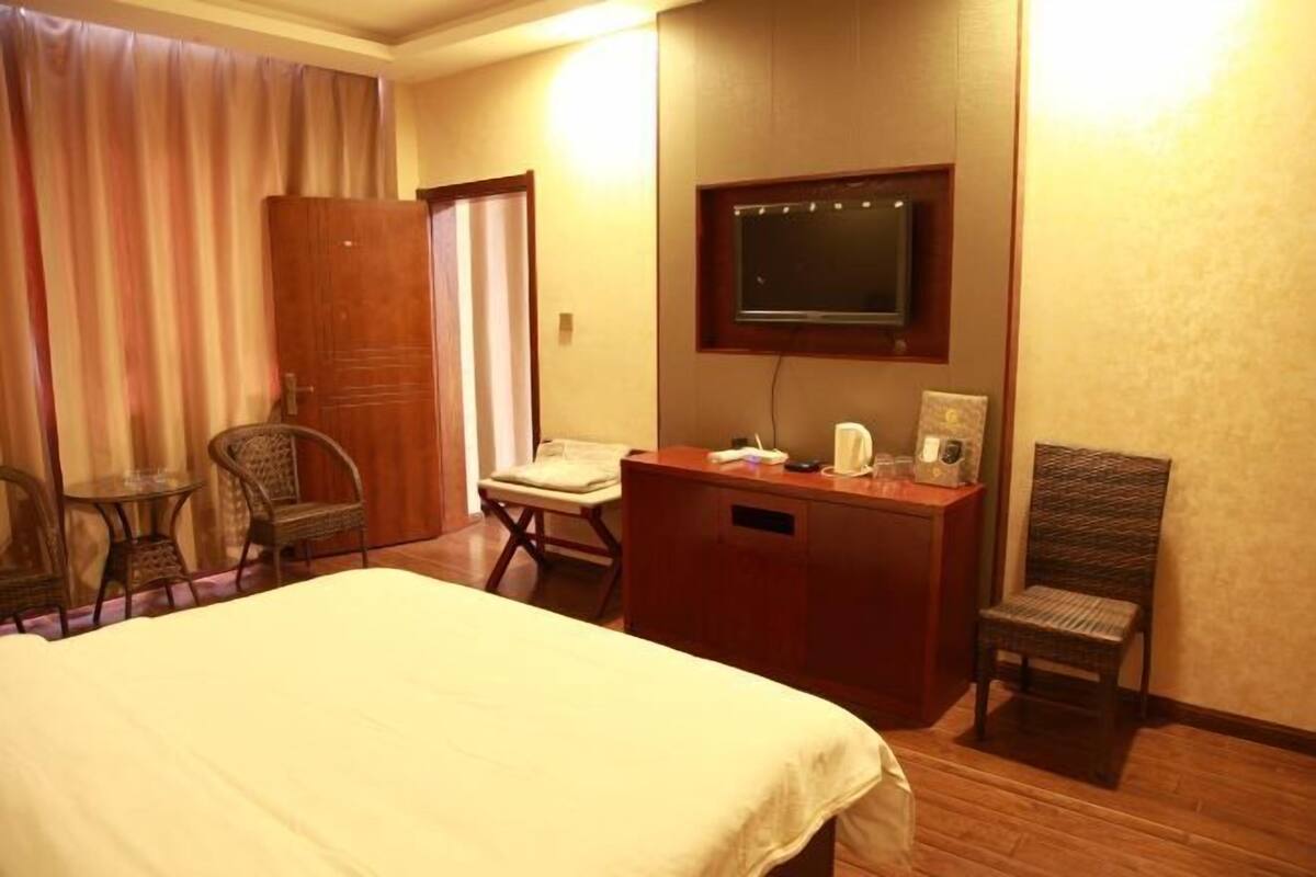 Hotelkamer met een bed, een bureau met een flatscreen televisie, twee rieten stoelen, een bijzettafeltje en een raam met gordijnen.