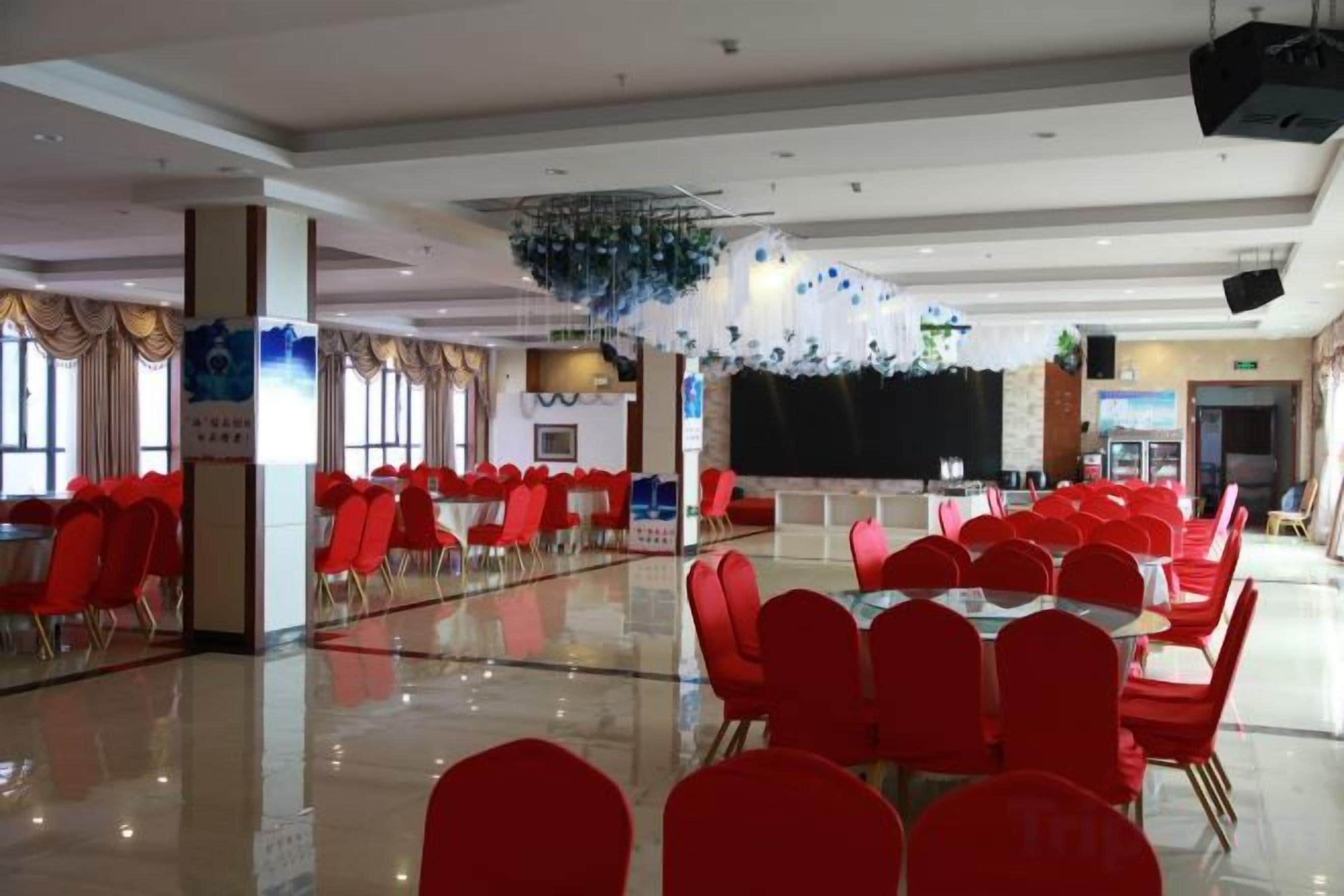 A banquet hall with rows of red chairs and tables, a stage, and a polished floor.