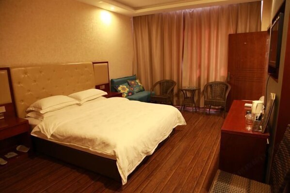 A hotel room with a large bed, a wooden floor, a desk with a chair, a television, and a window with curtains.
