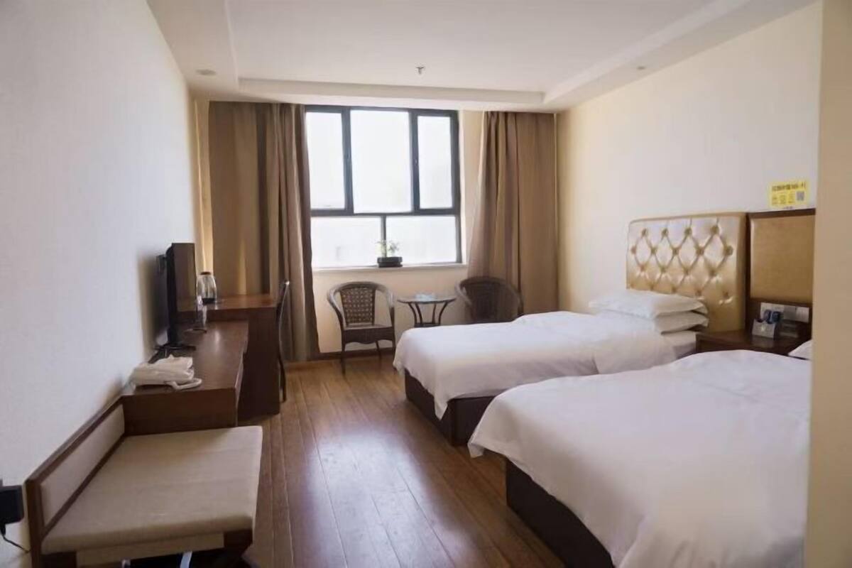 Een hotelkamer met twee bedden, een bureau, een stoel, een klein tafeltje en een raam met gordijnen.