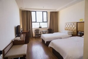 Hotellihuone, jossa on kaksi sänkyä, työpöytä, tuoli, pieni pöytä ja ikkuna, jossa on verhot.