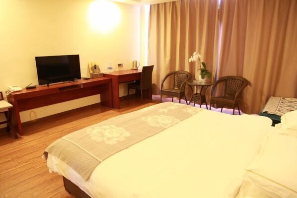 Ein Hotelzimmer mit Bett, Schreibtisch mit Fernseher, Stuhl, kleinem Tisch mit Pflanze und Fenster mit Vorhängen.