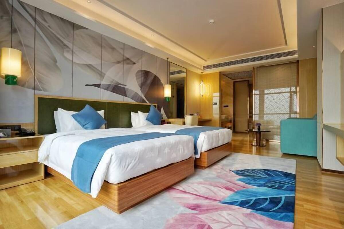 Une chambre d’hôtel avec deux lits, une grande fresque murale abstraite, un plancher en bois et une grande fenêtre agrémentée de rideaux à motifs.