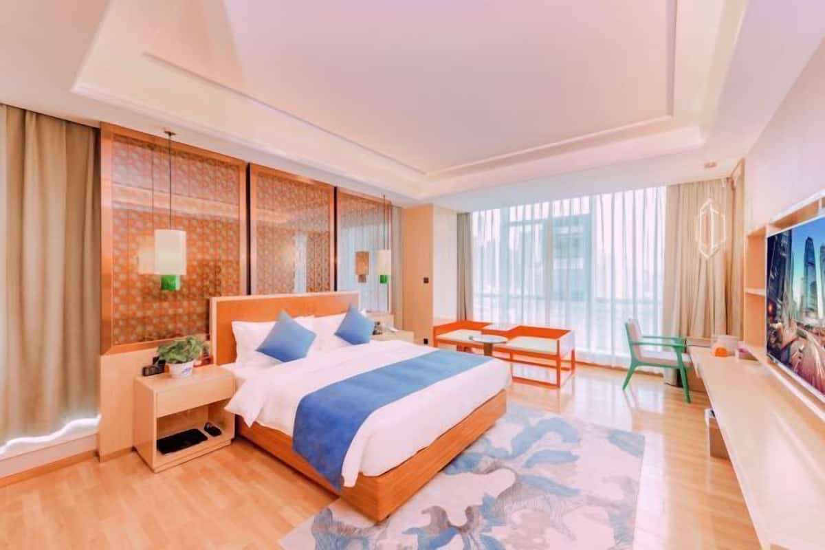 Une chambre d’hôtel avec un grand lit, un bureau avec une chaise, une télévision et une grande fenêtre avec des rideaux.