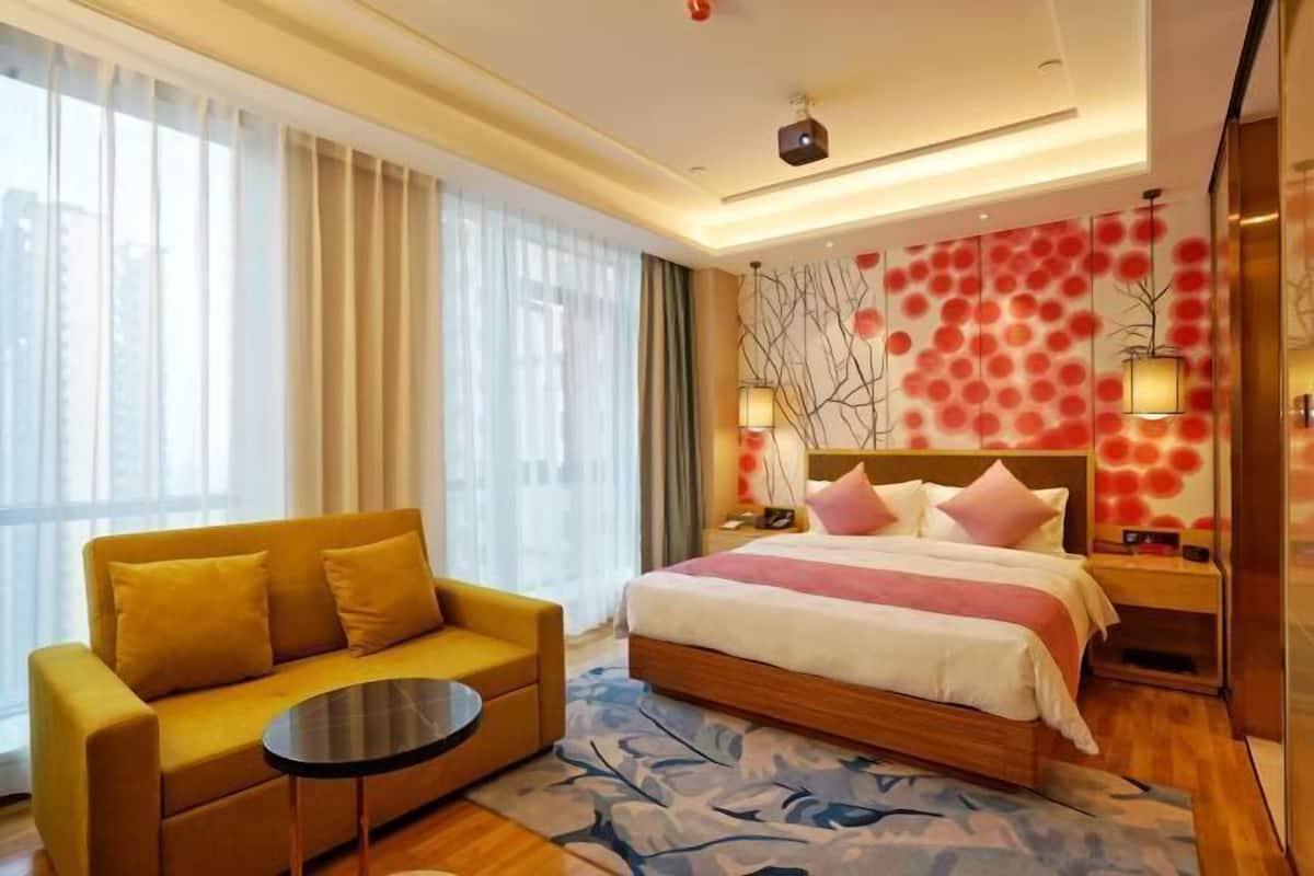 Une chambre d’hôtel avec un lit, un canapé, une petite table et une grande fenêtre avec des rideaux.