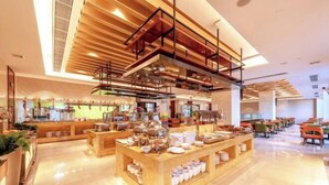 Una hall moderna di un hotel con una postazione caffè al centro, zone relax e una scala che conduce ai piani superiori.