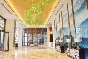 A hotel lobby with a polished floor, a reception desk, and a large wall with a mountainous landscape mural. - Wuhan Wellton Yiju Hotel (Wuhan)