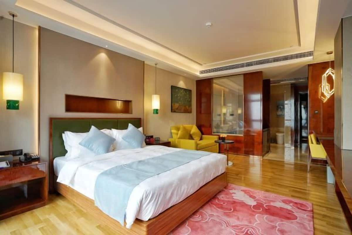 Une chambre d’hôtel avec un grand lit, des tables de chevet, une chaise, un miroir et une vue sur le couloir.