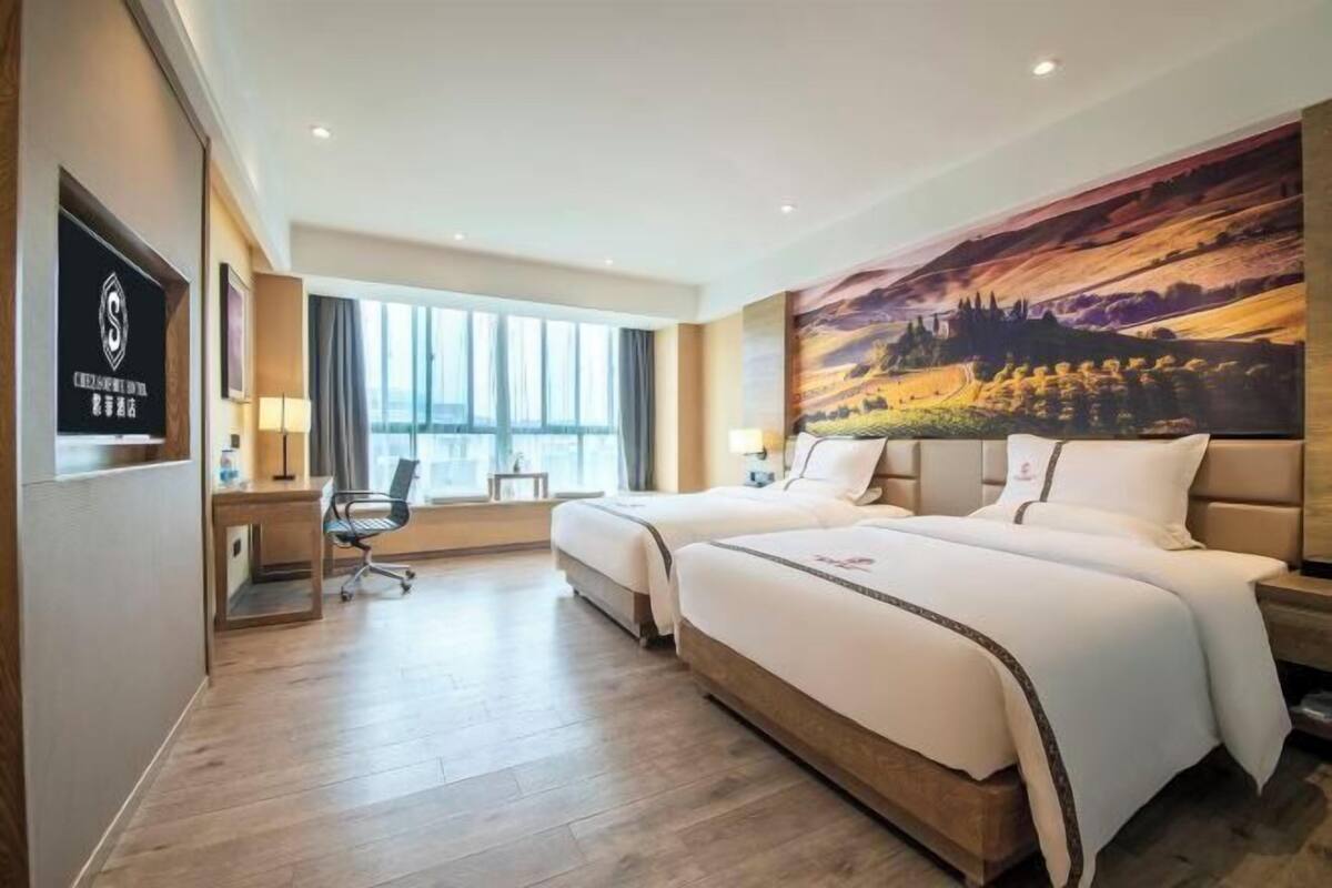 A hotel room with two beds, a desk, a chair, and a large window.