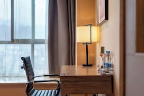 Et hotelværelse med et træskrivebord, en sort læderstol, en lampe og en vandflaske.