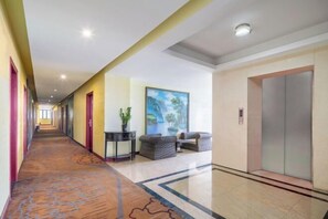 A hotel corridor with a carpeted floor, a painting on the wall, a sofa, and an elevator.