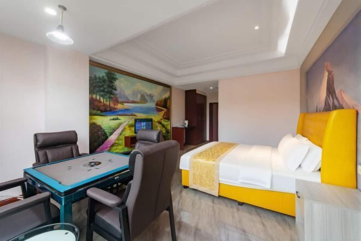 Habitación de hotel con cama, escritorio con sillas, un cuadro en la pared y puerta que da a otra habitación.
