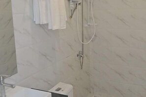 Un baño con un lavamanos blanco, un cabezal de ducha de mano y un panel de control.