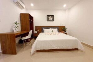 A bedroom with a bed, a desk, a chair, a wardrobe, a bedside table, and a wall-mounted air conditioner.