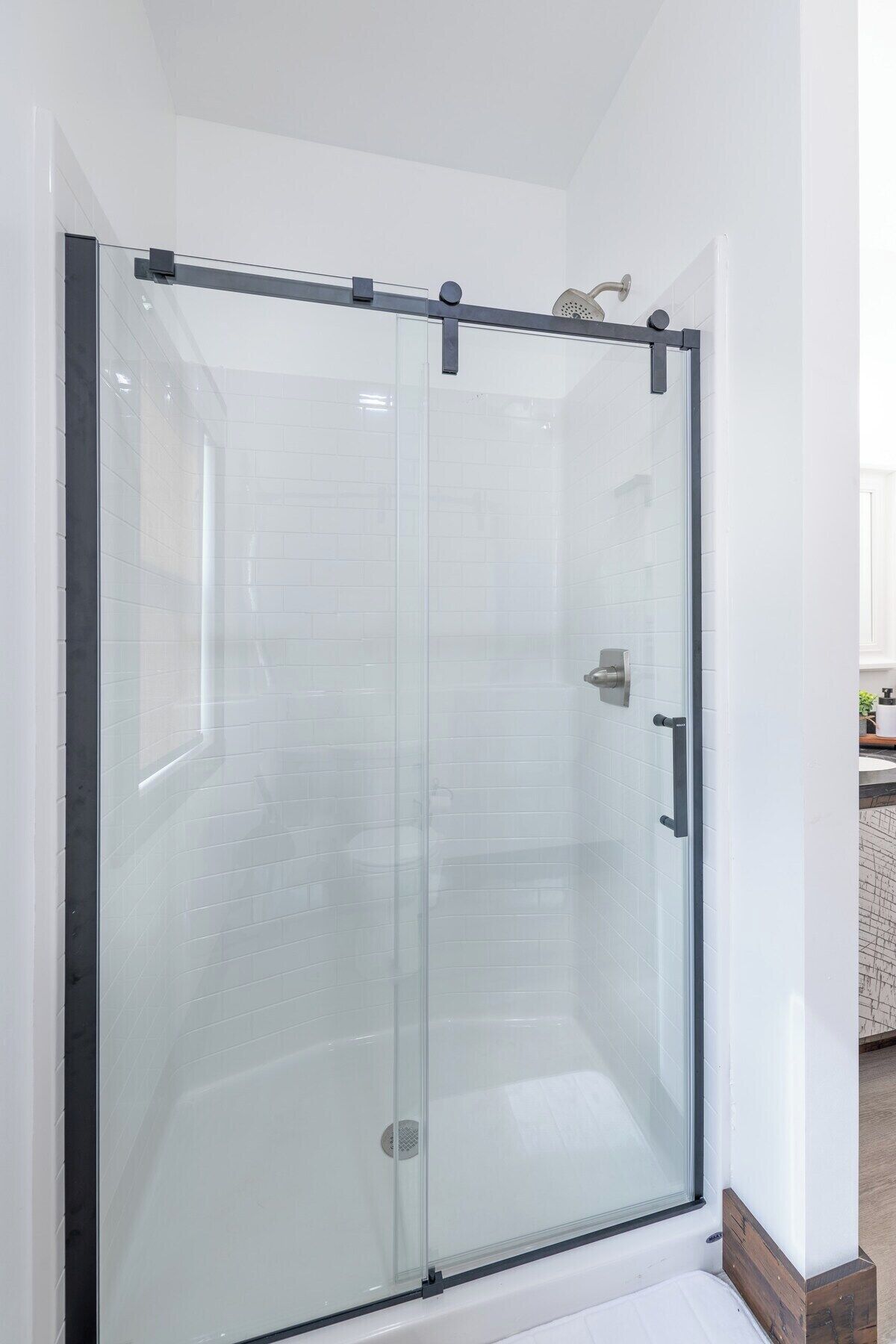 A glass-enclosed shower with a sliding door, white tiled walls, and a visible bathroom counter with a sink.