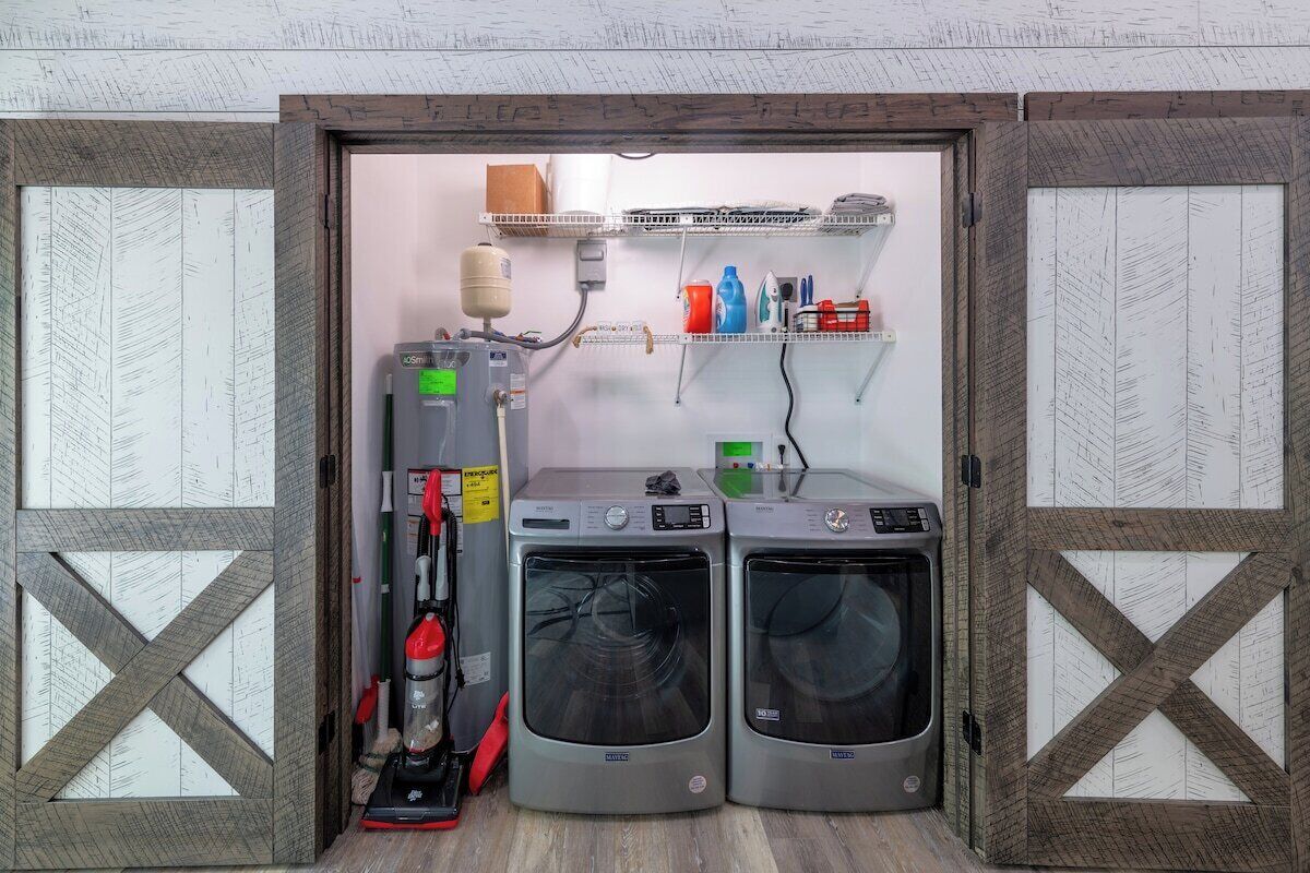 A laundry area with two front-loading washing machines, a stacked washer and dryer, and a vacuum cleaner.