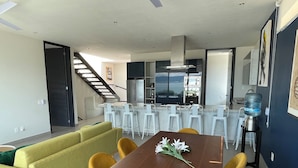 Ein modernes Wohnzimmer mit einem Holzesstisch, gelben Stühlen, einem grünen Sofa und einer Küchenzeile mit weißen Barhocker.