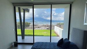 Ein Schlafzimmer mit einem großen Bett, Blick auf eine grüne Wiese und einen Berg durch eine Glastür.