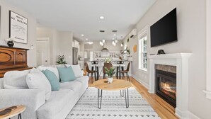 A modern living room with a fireplace, a dining area, and a kitchen in the background.