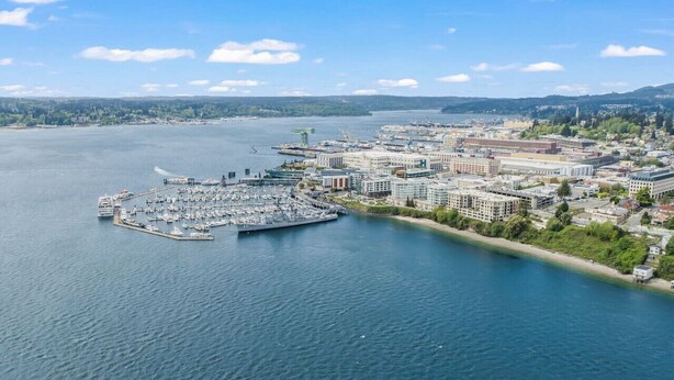 An aerial view of a coastal city with a marina, buildings, and a clear sky.