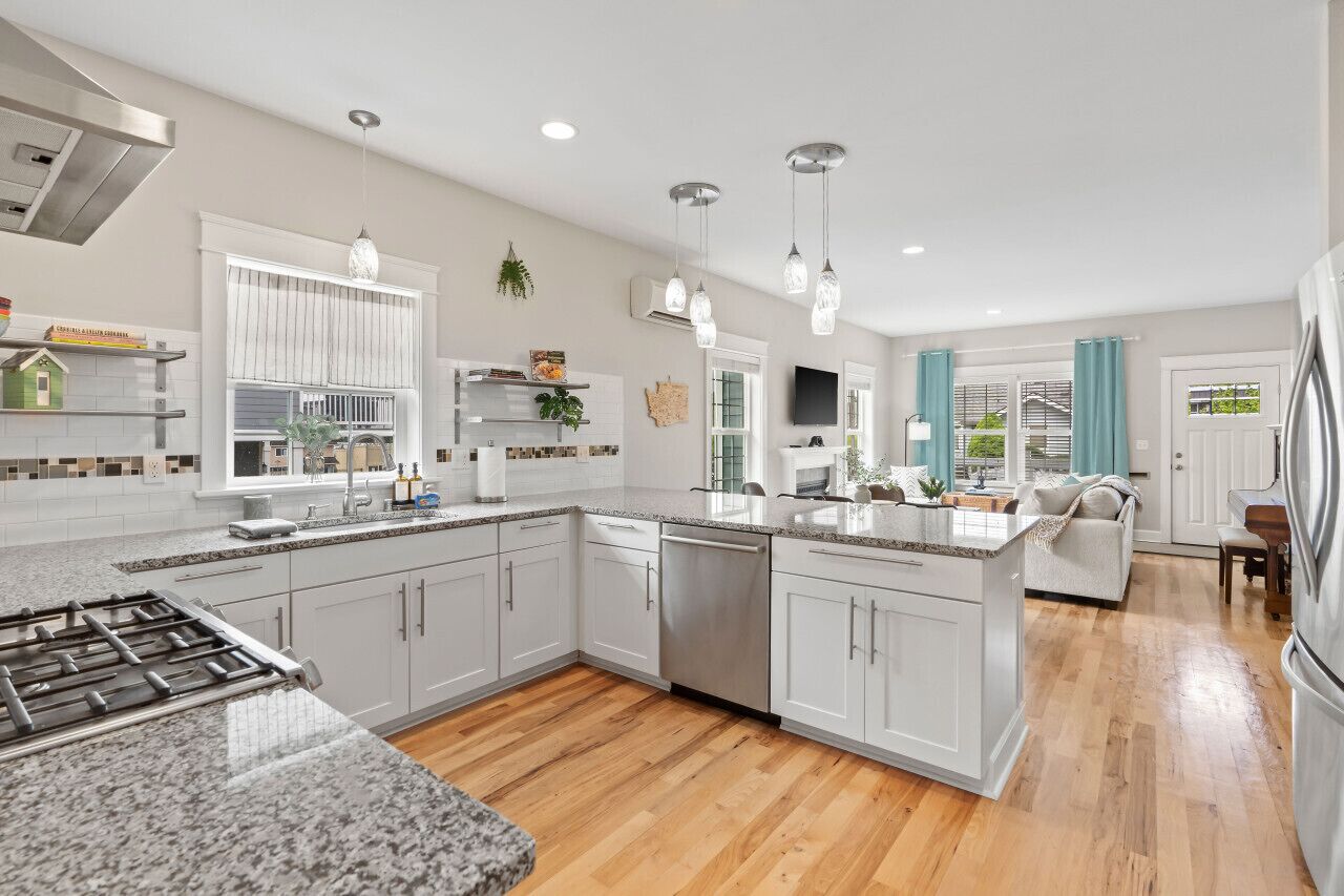 A modern kitchen with white cabinets, granite countertops, stainless steel appliances, and pendant lighting.
