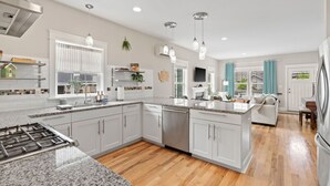 A modern kitchen with white cabinets, granite countertops, stainless steel appliances, and pendant lighting.