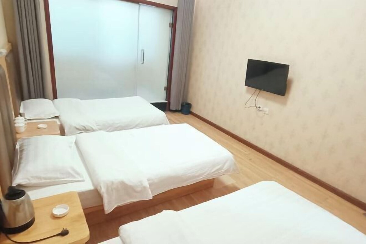 Habitación de hotel con dos camas individuales, un televisor montado en la pared, piso de madera y una mesita con tetera y tazas.