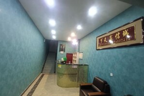 Un área de recepción con mostrador, un cartel enmarcado, una escalera y una zona de estar.