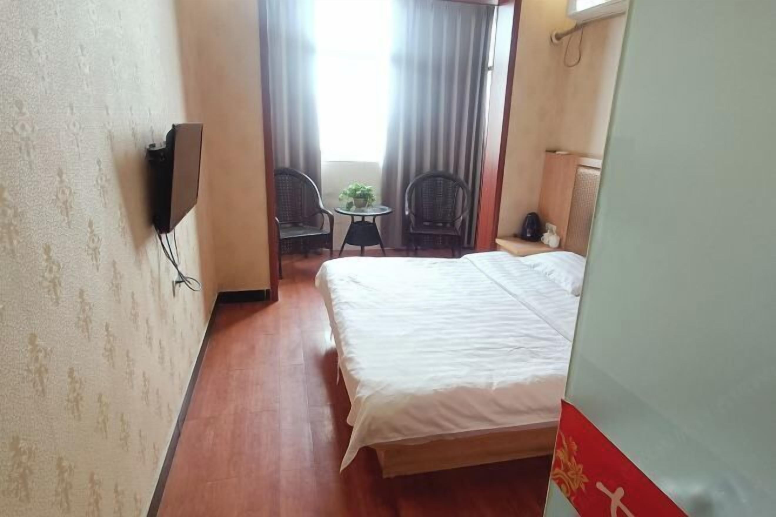 Quarto de hotel com cama, televisão na parede, mesa pequena com cadeiras e janela com cortinas.