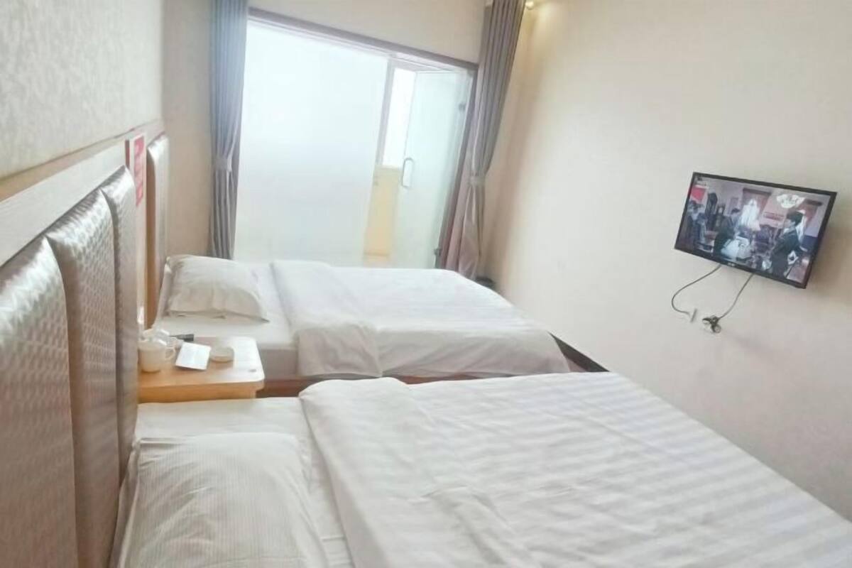A hotel room with two beds, a television on the wall, and a window with curtains.