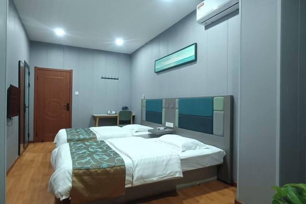 A hotel room with two beds, a desk, a chair, a TV, and a window.