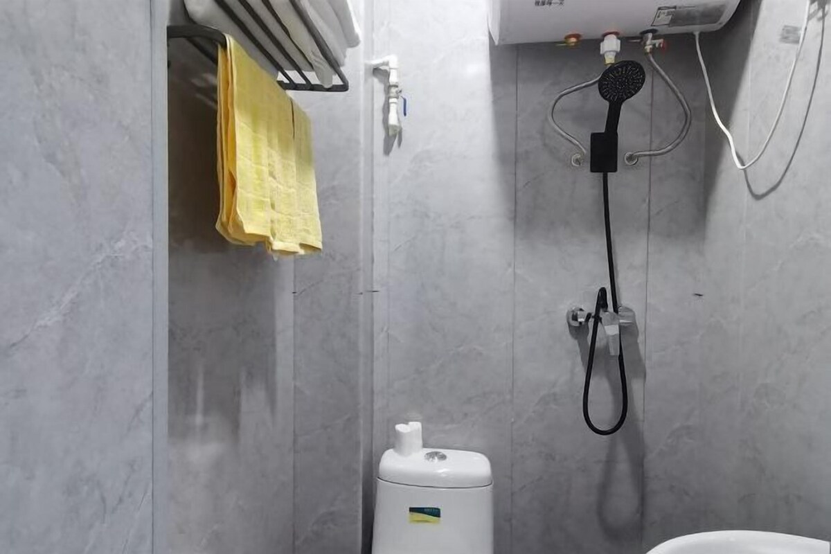 Un baño con ducha, toallero y una toalla amarilla, además de un inodoro.