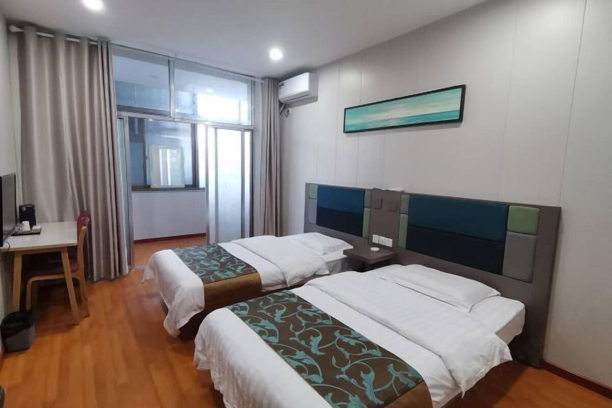 A hotel room with two beds, a desk, a chair, and a window with curtains.