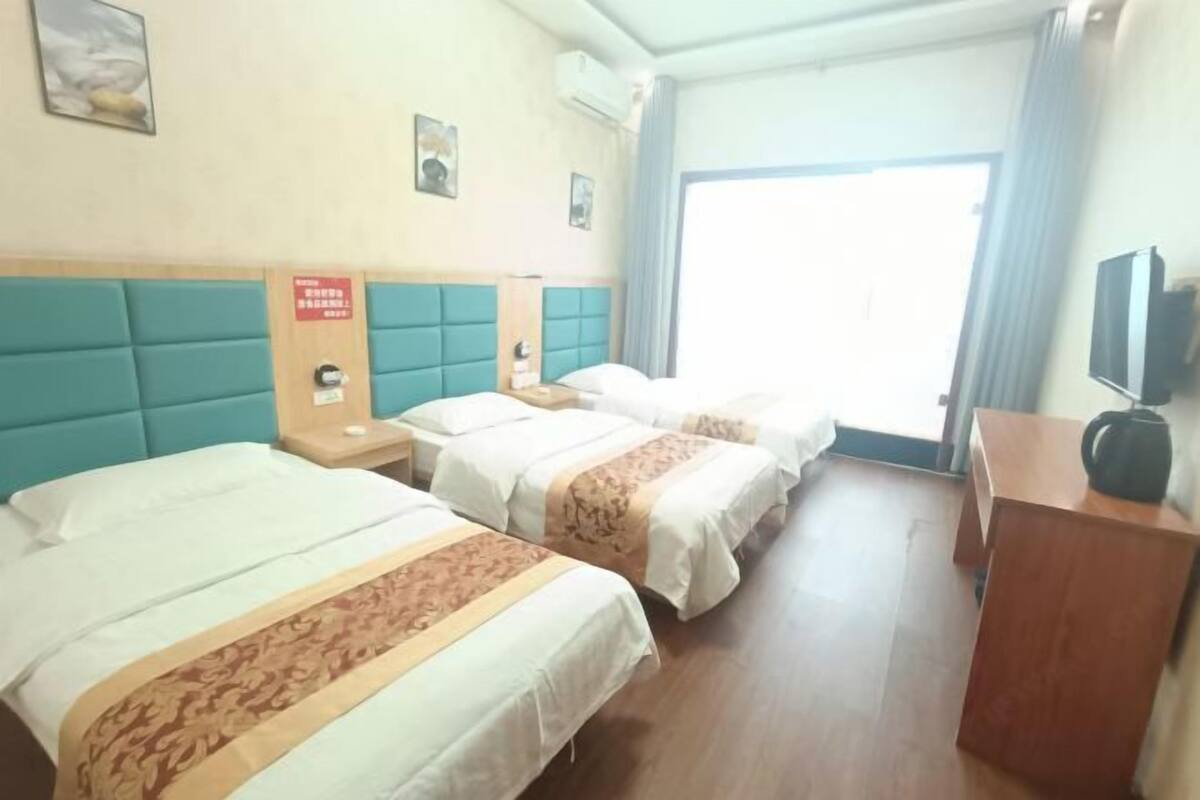 A hotel room with two beds, a wooden desk, a television, and a window with curtains.