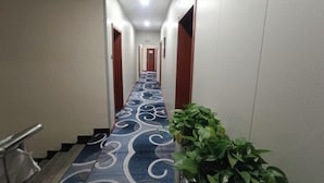 A hotel hallway with a patterned carpet, wooden doors, and a potted plant. - Qiqi Hotel (Taiyuan Zhenwu Road Wanmaqi Square) (Taiyuan)