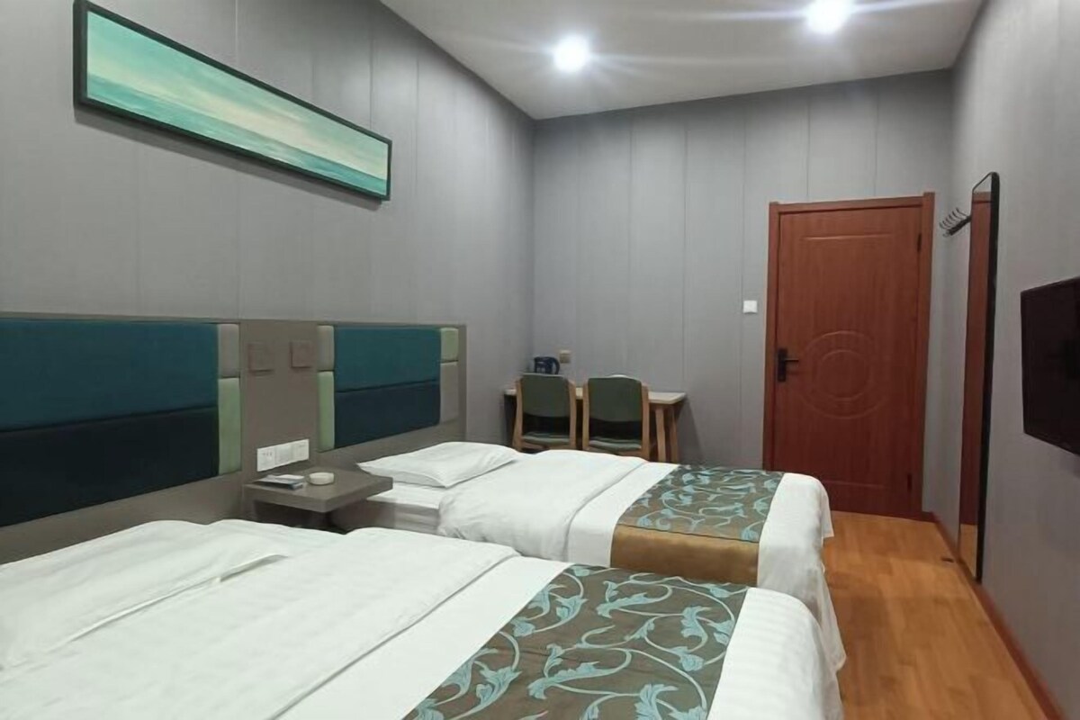 Habitación de hotel con dos camas, un escritorio, sillas, un televisor y una puerta.