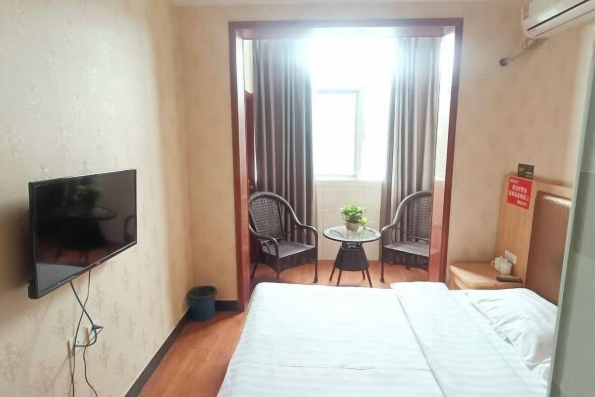 A hotel room with a bed, a TV, a small table with chairs, and a window with curtains.