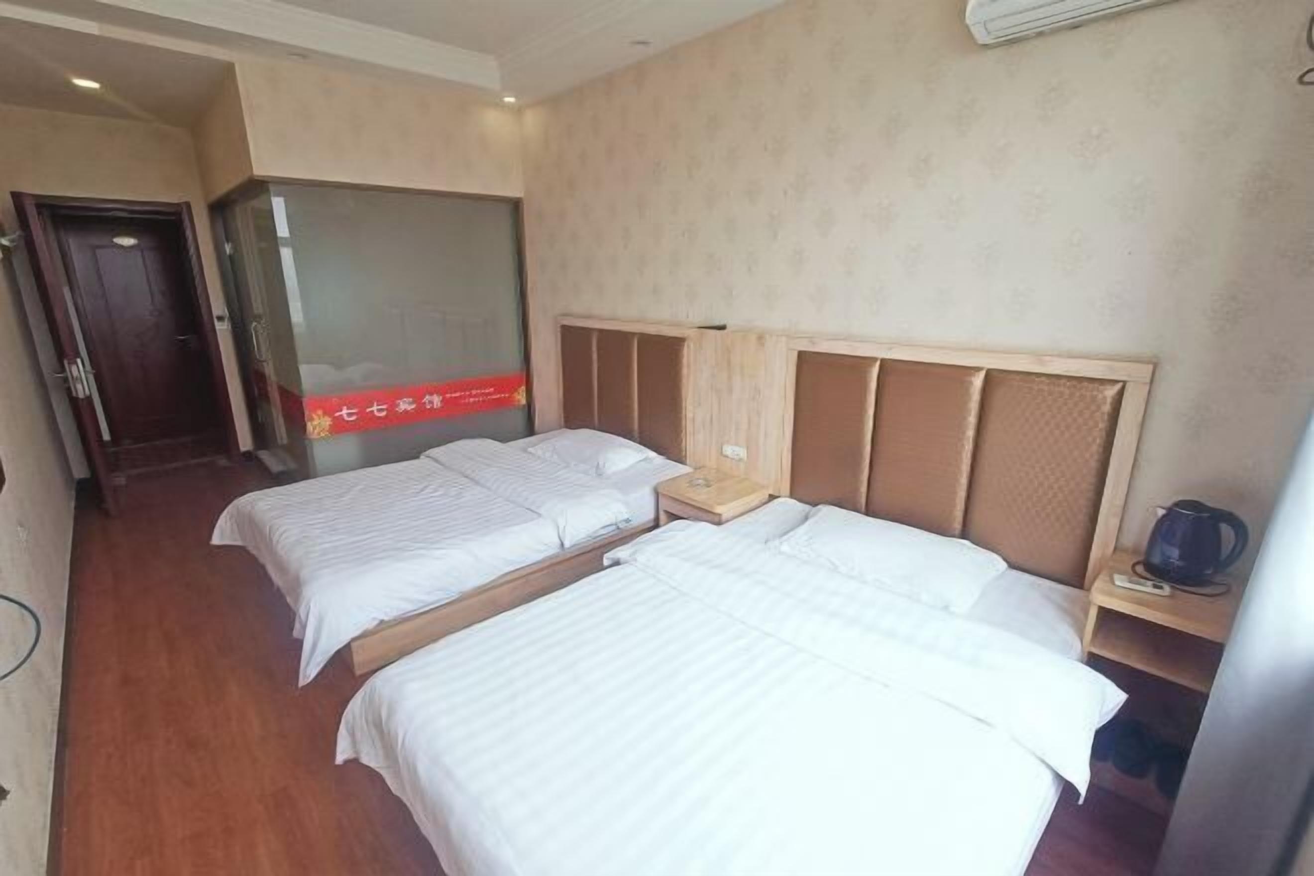 Quarto de hotel com duas camas, uma cabeceira de madeira, uma mesa de cabeceira e um ar condicionado fixado na parede.