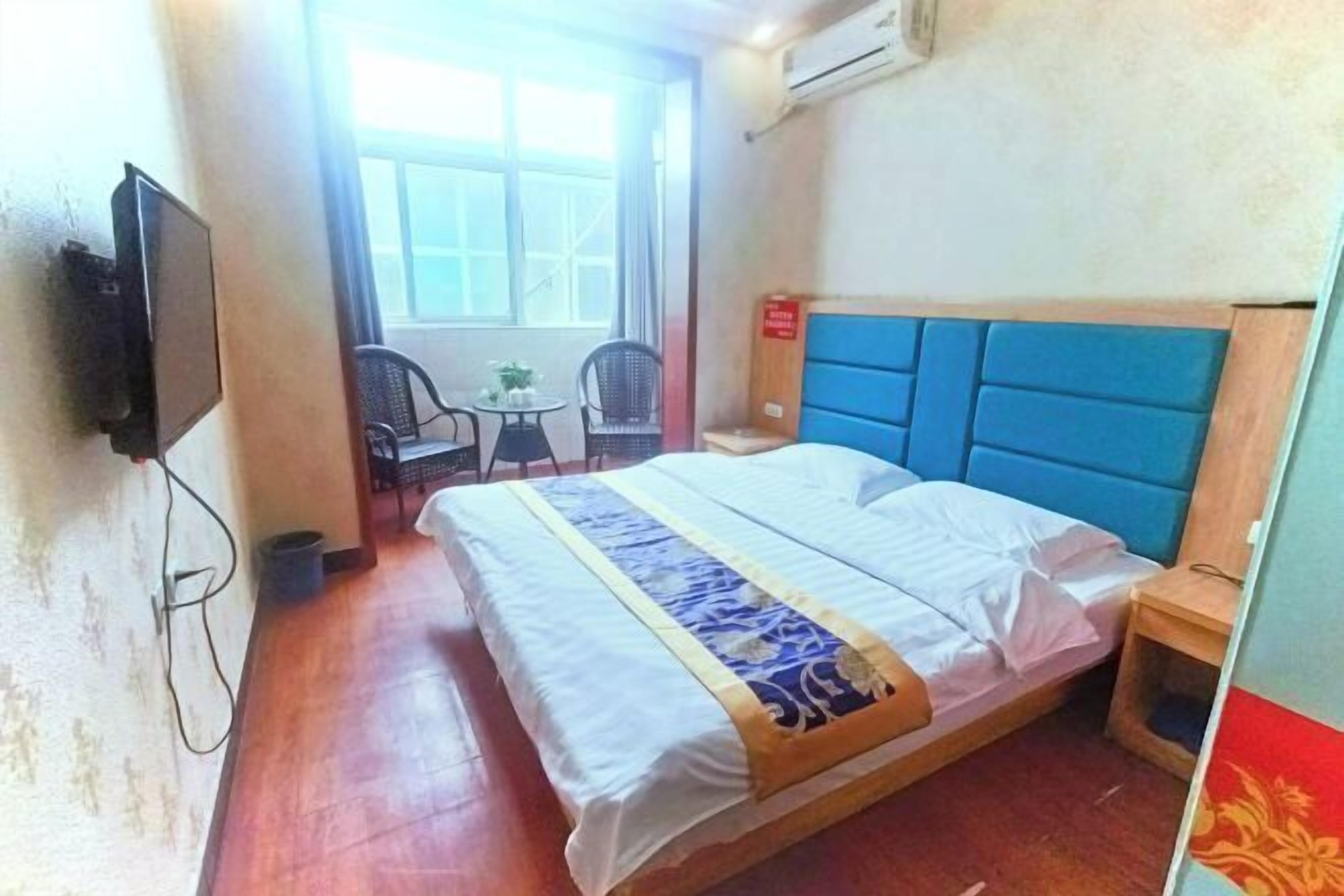 A hotel room with a bed, a TV, a small table with chairs, and a window.